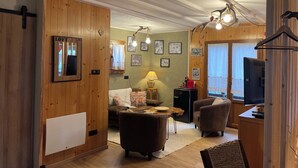 A cozy loft-style room with wooden walls, a sofa, a coffee table, and a TV. - Le Chalet du Coeur (Mittlach)