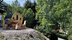 A rustic wooden structure with a curved roof, surrounded by lush greenery and trees. - Le Chalet du Coeur (Mittlach)