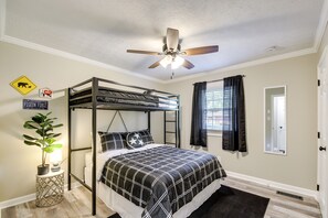 Un dormitorio con literas, ventilador de techo, planta en maceta y cama con colcha a cuadros blanco y negro.