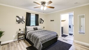 A bedroom with a bed, a ceiling fan, a window with curtains, and a hallway leading to another room. - Backyard Family Oasis w/ Fire Pit + Deck, By Dwtn (Knoxville)