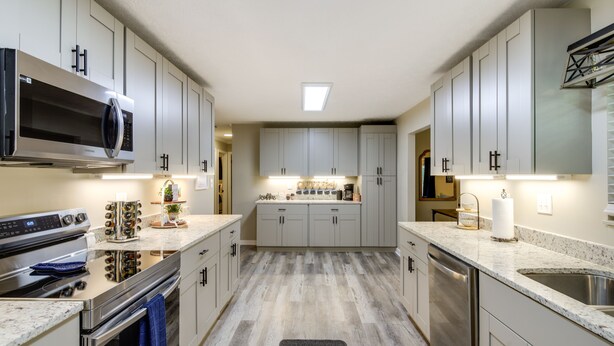 A modern kitchen with stainless steel appliances, light wood flooring, and a central island with a sink. - Backyard Family Oasis w/ Fire Pit + Deck, By Dwtn (Knoxville)