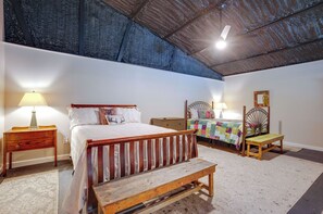 Cozy retreat with a large bed, bedside table, and bench, set against a rustic ceiling with exposed beams.