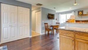 A kitchen with wooden cabinets, a dining table with chairs, a TV mounted on the wall, and a window with curtains. - 12 Mi to Denver: Golden Vacation Rental! (Golden)