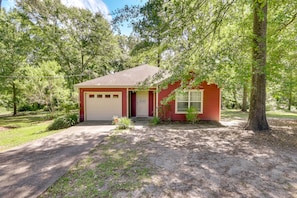 A single-story house with a red exterior, a garage, and a front yard with trees and a driveway.