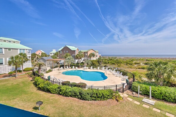 A residential area with a swimming pool surrounded by lounge chairs and a fence.