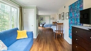 A room with a blue sofa, a wooden dresser, and a television. There is a bed with a blue and white patterned bedspread in the background. - Haven in the trees, minutes from hiking trails (Mill Valley)