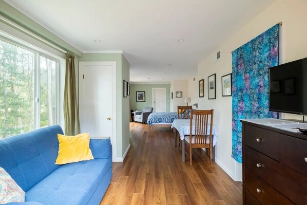A room with a blue sofa, a wooden dresser, and a television. There is a bed with a blue and white patterned bedspread in the background. - Haven in the trees, minutes from hiking trails (Mill Valley)