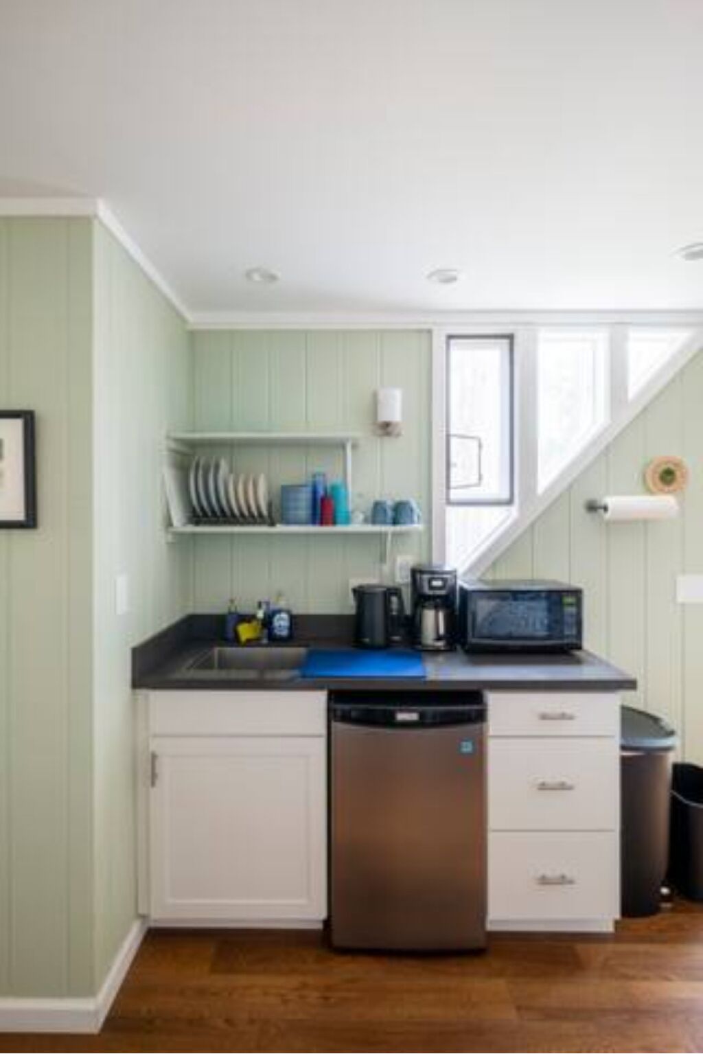 Una cocina compacta con alacenas blancas, lavavajillas, microondas y cafetera.
