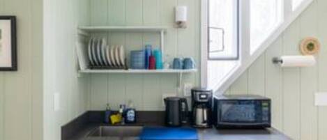 Una cocina compacta con alacenas blancas, lavavajillas, microondas y cafetera.