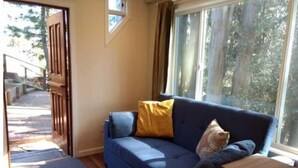 A room with a blue sofa, a small wooden table, and a view of trees through a window. - Haven in the trees, minutes from hiking trails (Mill Valley)
