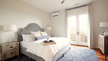 A bedroom with a bed, nightstands, a ceiling fan, an air conditioning unit, and a view of the outside through a sliding glass door.