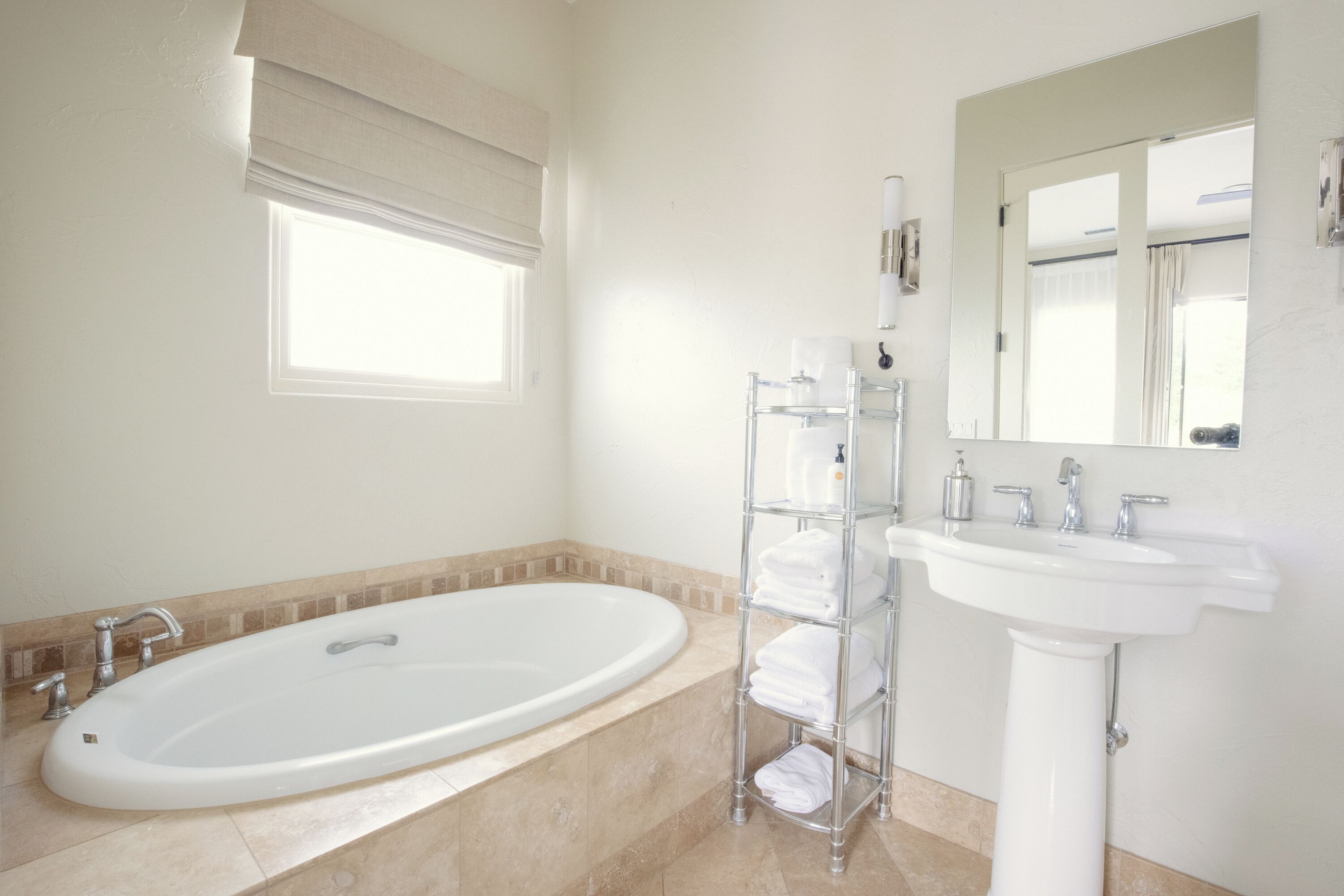 A bathroom with a bathtub, a sink, a towel rack, and a window with blinds.