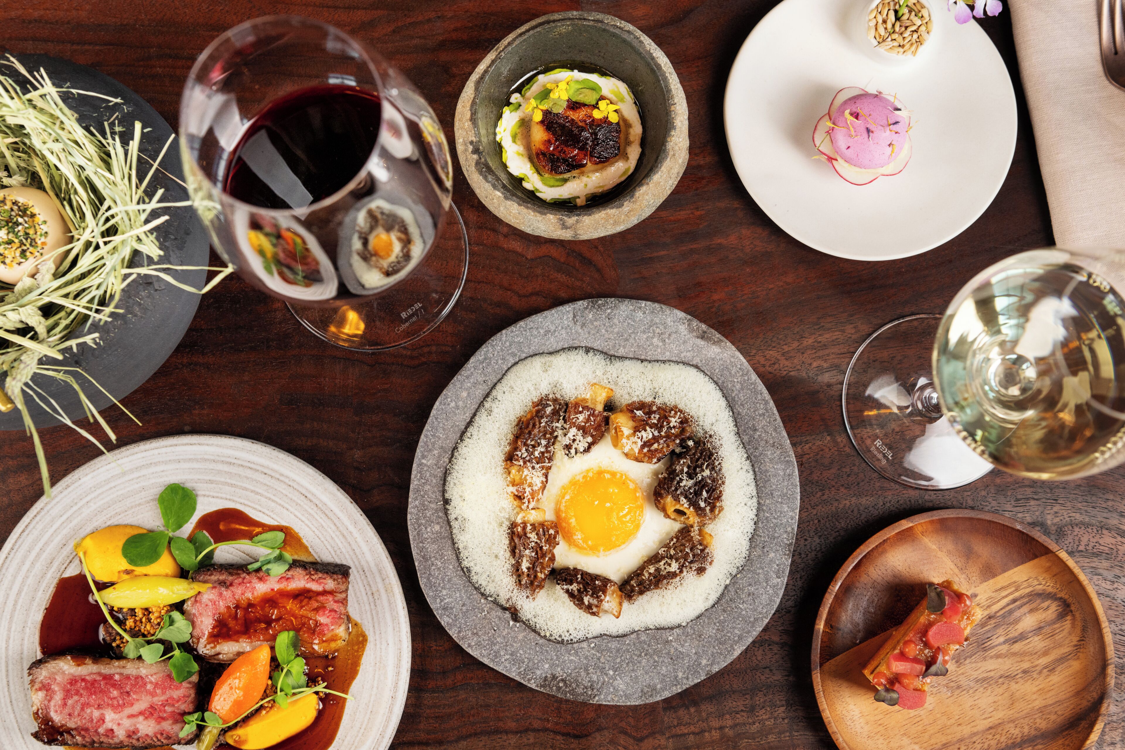 A dining table with various dishes, wine glasses, and a wooden bowl.