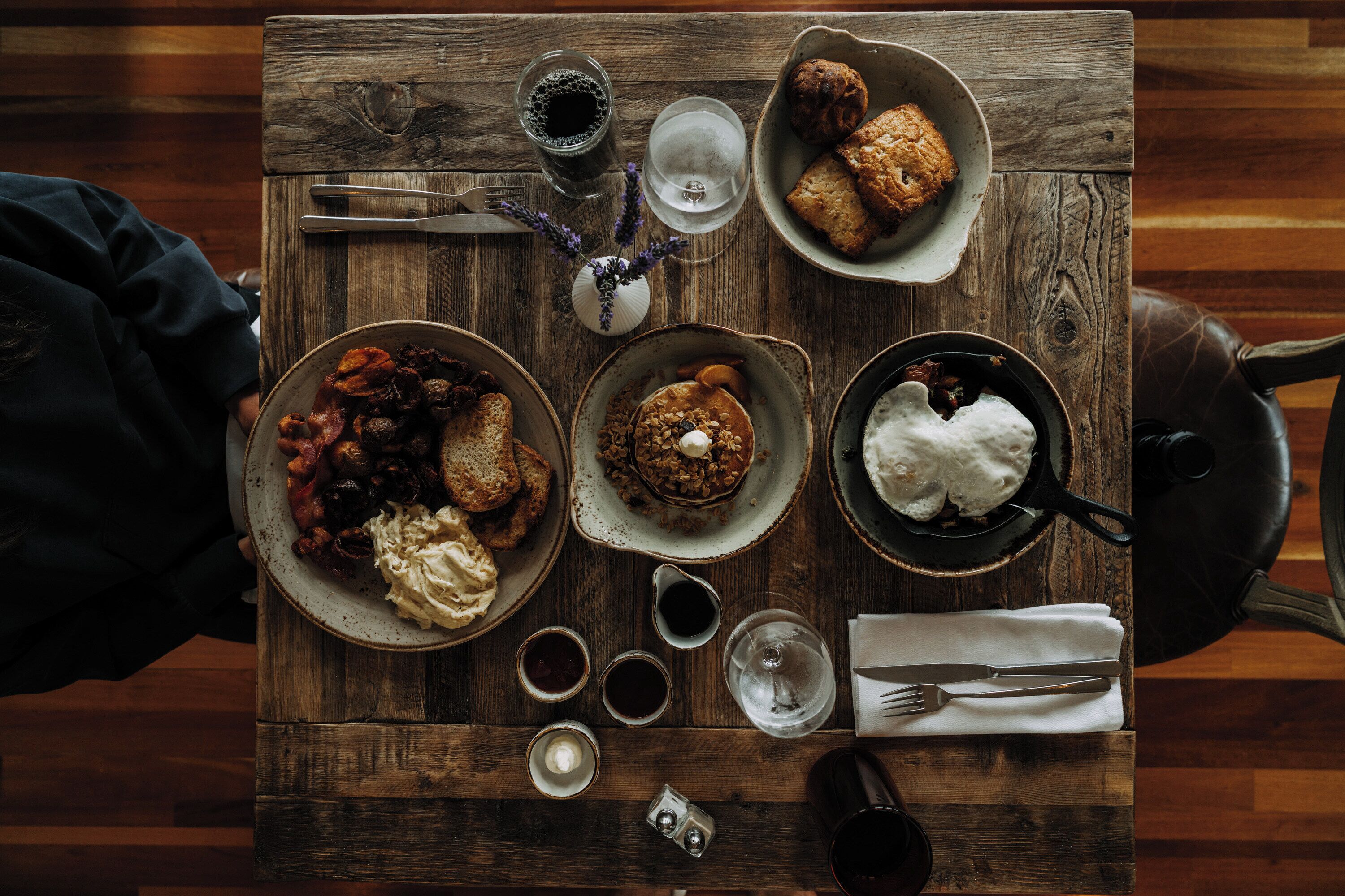 A wooden table with various dishes, cutlery, and glasses, suggesting a dining setting.