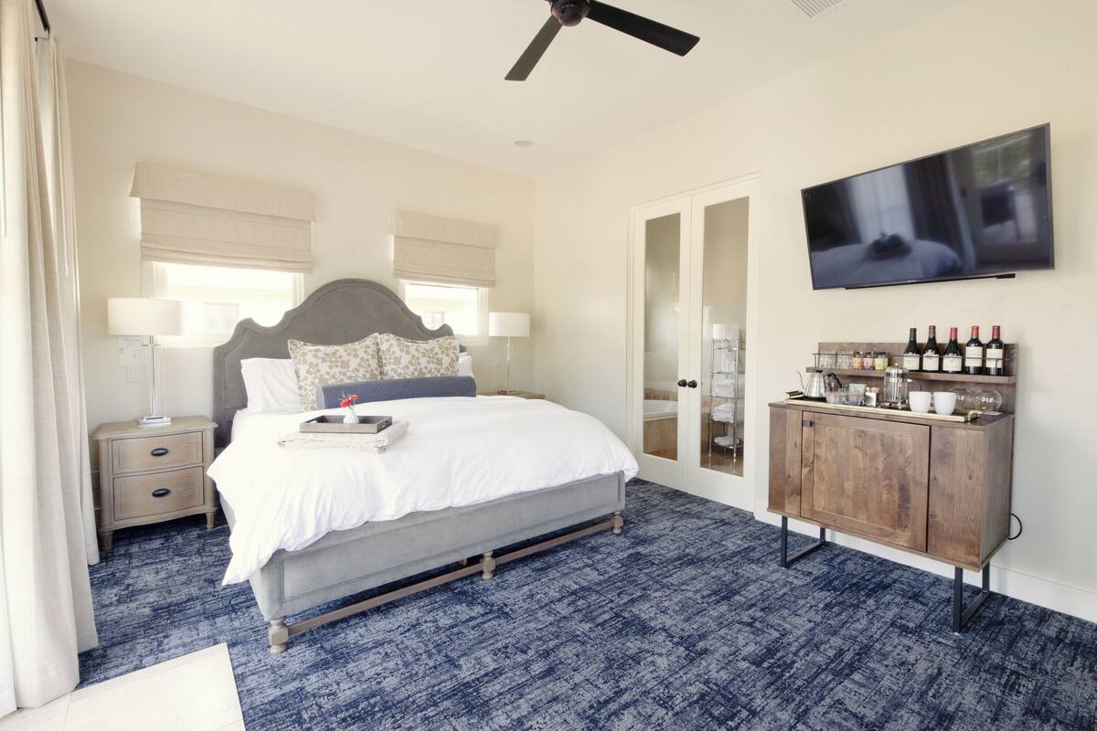 A bedroom with a bed, bedside tables, a TV, and a minibar.