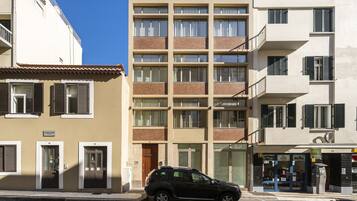 En bygning med flere etager, en beige facade og flere balkoner, med en sort bil parkeret foran.