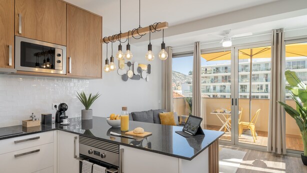 Een moderne keuken met een centraal eiland, een ingebouwde magnetron en hangende lampen.