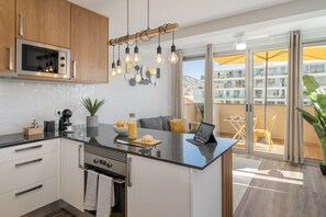 A modern kitchen with a central island, built-in microwave, and hanging light fixtures. - Holidays in Funchal - Alegria Flat II (Funchal)