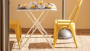 Een balkon met een ontbijttafel, gele stoelen en een gebouw op de achtergrond.