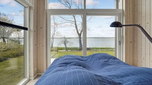 A bedroom with a large window, a bed with a blue blanket, and a nightstand with a lamp.