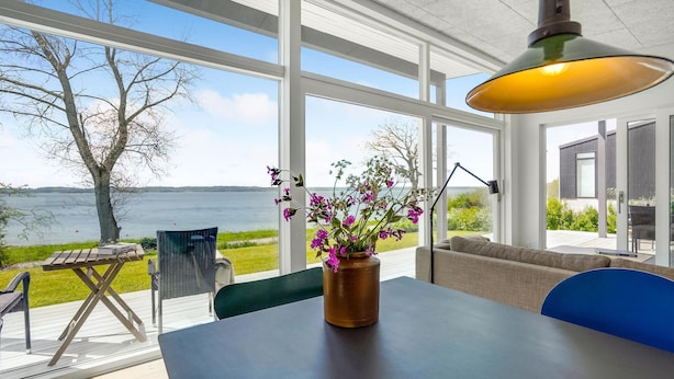 A modern room with large windows overlooking a lake, a table with a vase of flowers, and a sofa.