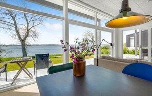 Une chambre moderne avec de grandes fenêtres donnant sur un lac, une table ornée d’un vase de fleurs et un canapé.