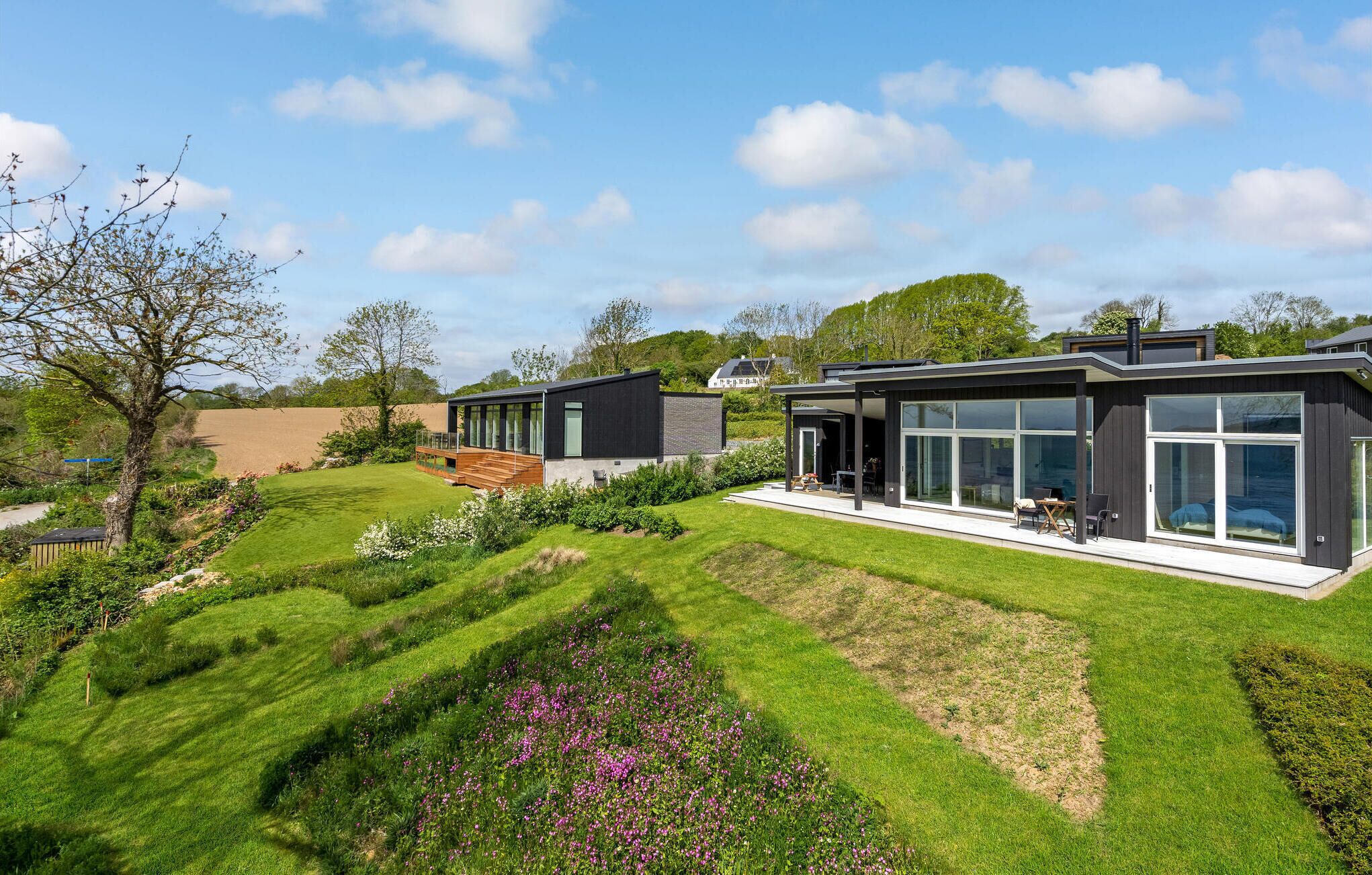 Ein modernes Haus mit großer Glasfassade, einer Terrasse und einem gepflegten Garten.