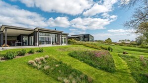 A modern house with a covered patio, a well-maintained lawn, and a garden with various plants and flowers.