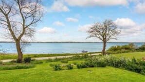 A grassy area with a pathway leading to a body of water, a boat, and two trees.
