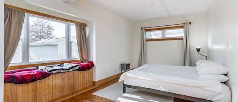 A bedroom with a bed, wooden floor, window with curtains, and a small bedside table.