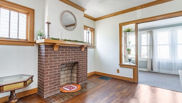 A room with a brick fireplace, wooden beams, a large window, and a sliding glass door. - Home of the Braves - Bradley Campus Suite (West Peoria)