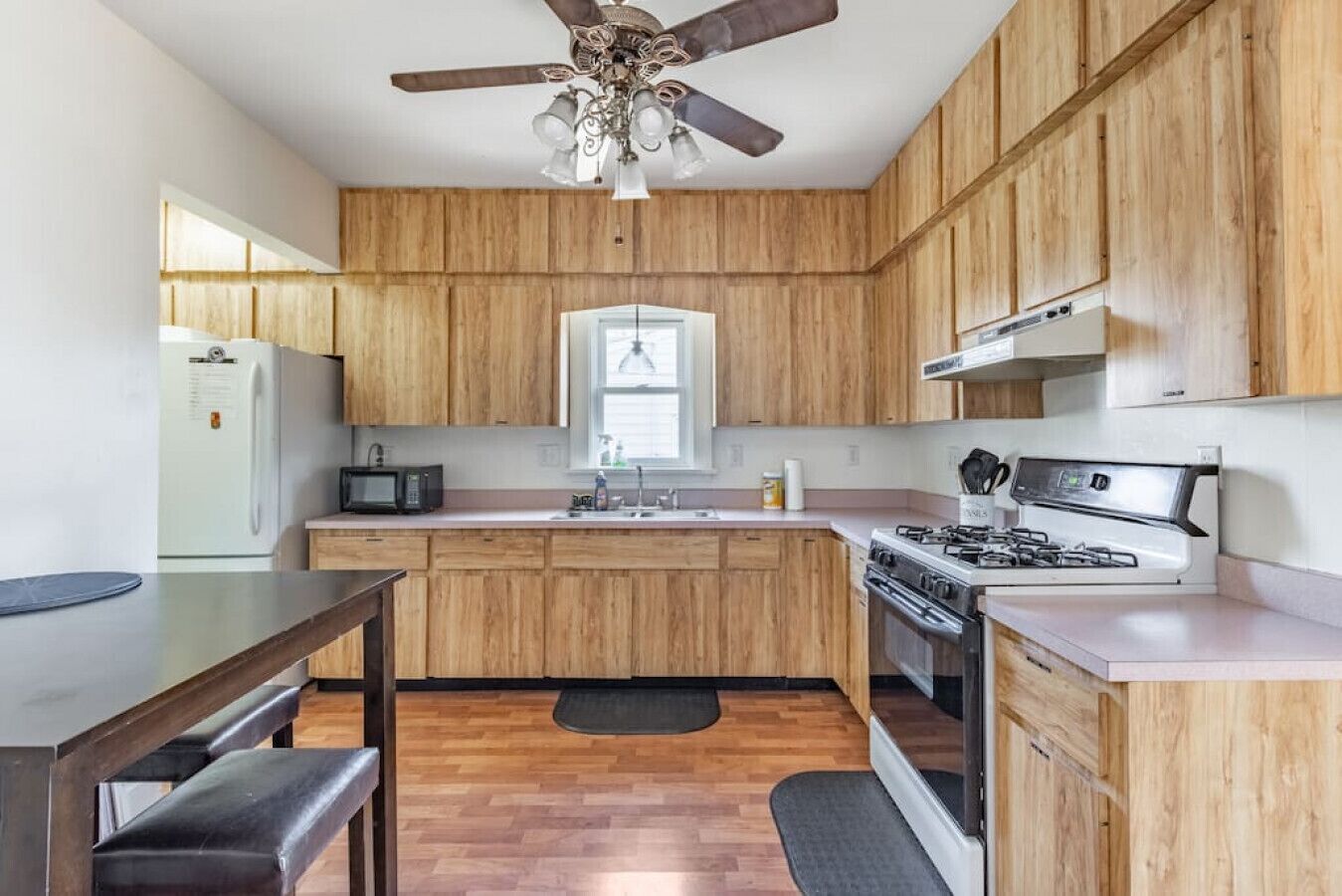 A kitchen with wooden cabinets, a microwave, a stove, and a ceiling fan.