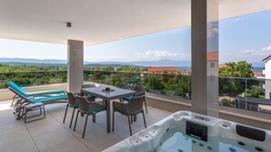 Ein Balkon mit Tisch und Stühlen, einem Whirlpool und Blick auf Meer und Berge.