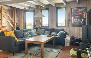 Ein gemütliches Wohnzimmer mit Holzbalkendecke, einer Sofagarnitur, einem Couchtisch und einem großen Fenster mit Blick.