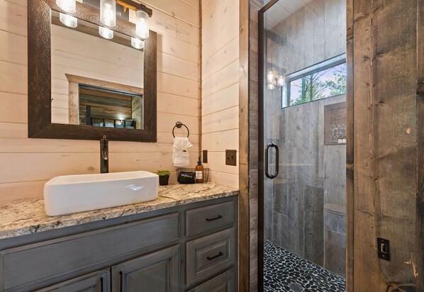A modern bathroom with a granite countertop, a large mirror, and a glass-enclosed shower.