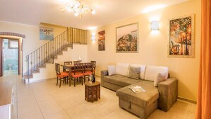 A living room with a sofa, dining table, chairs, a staircase, and artwork on the walls.