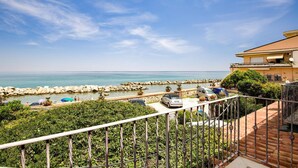 A coastal property with a view of the sea, a stone wall, and a balcony with potted plants.