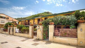 A courtyard with a paved floor, a gated entrance, and a building with a yellow facade and green roof.