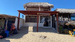 En byggnad vid stranden med ett halmtak, en skylt med texten ”CABANAS EL TRIBOL” och en trappa som leder upp till en övre våning.