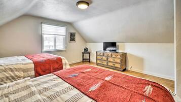 A bedroom with two beds, a dresser, a television, and a window.