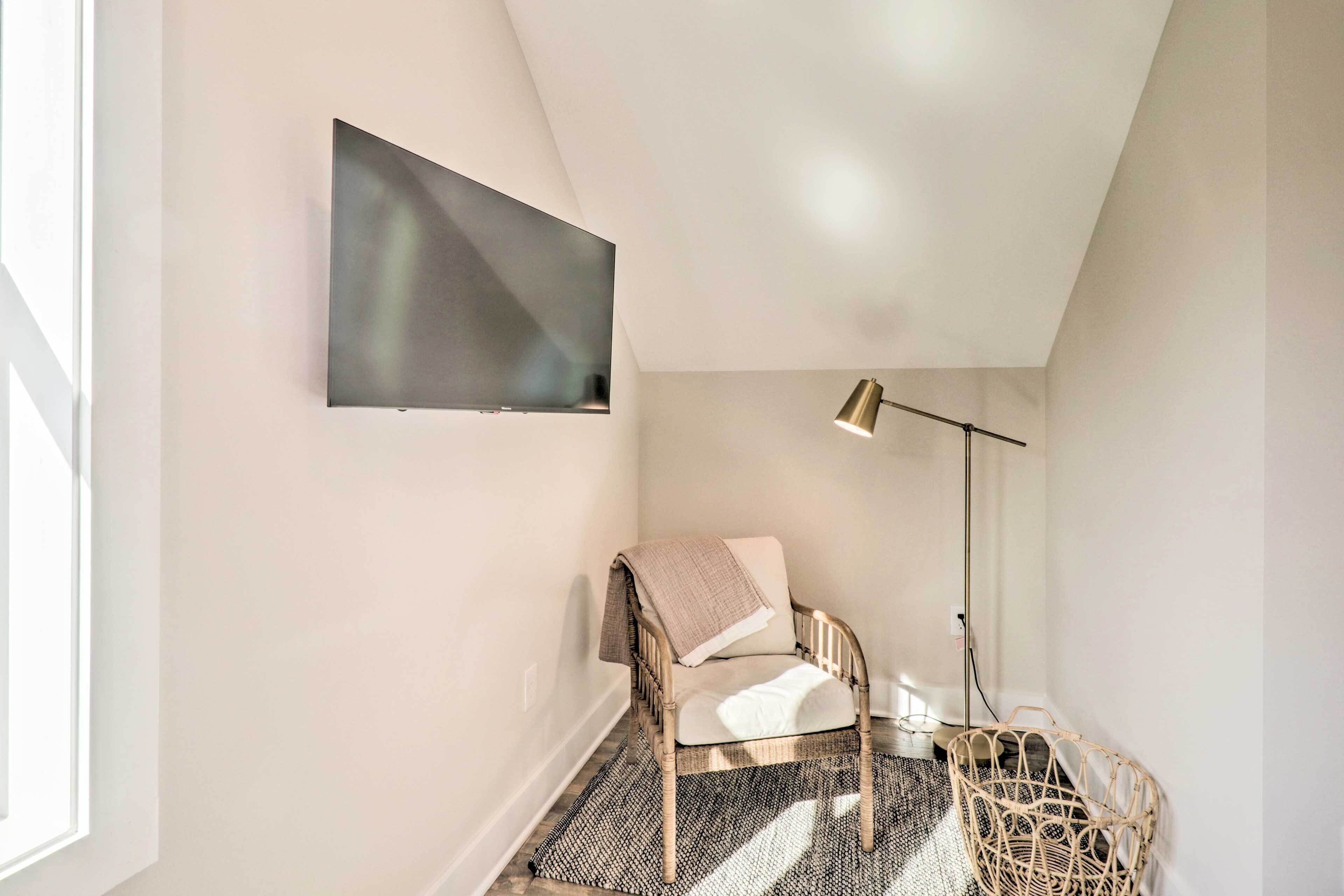 Una habitación moderna con cama, televisor de pared, lámpara de pie y silla de mimbre.