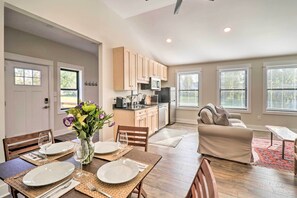 Un coin repas avec une table dressée pour quatre personnes, une cuisine en arrière-plan et un salon avec un canapé et une table basse.