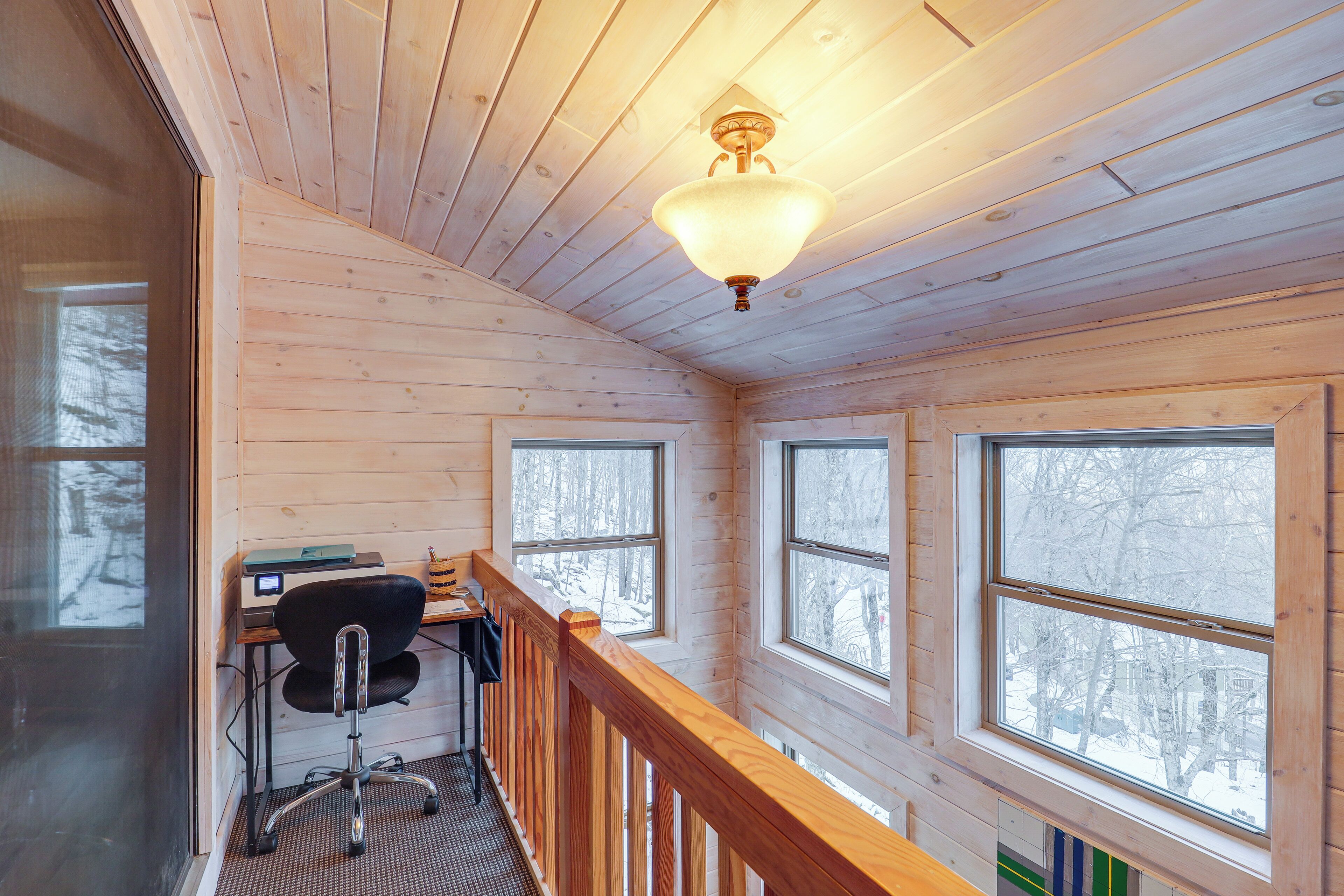 A wooden cabin interior with a desk, chair, and large windows.