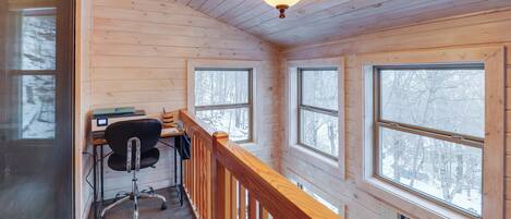 A wooden cabin interior with a desk, chair, and large windows.