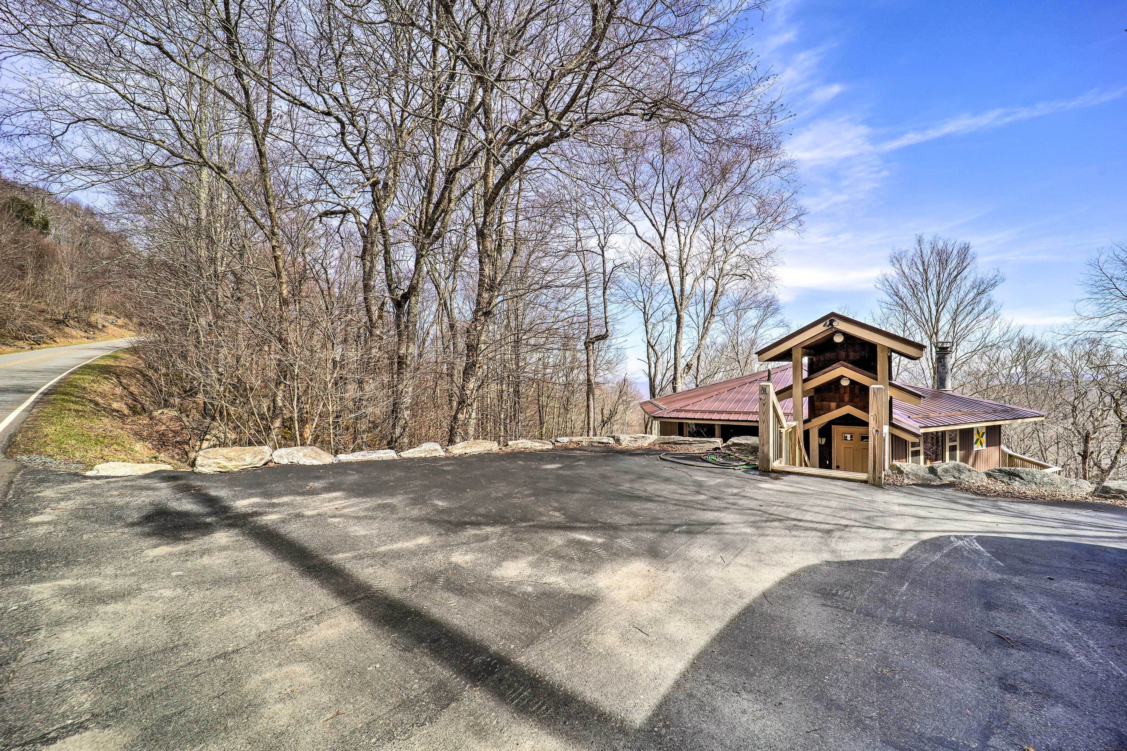 Un chalet avec un toit rouge, entouré d’arbres et bordé d’une route goudronnée.