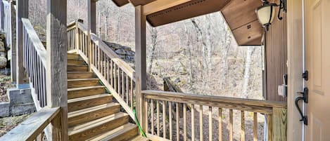 A wooden staircase leading to a covered porch with a railing, a lantern, and a view of a forested area.