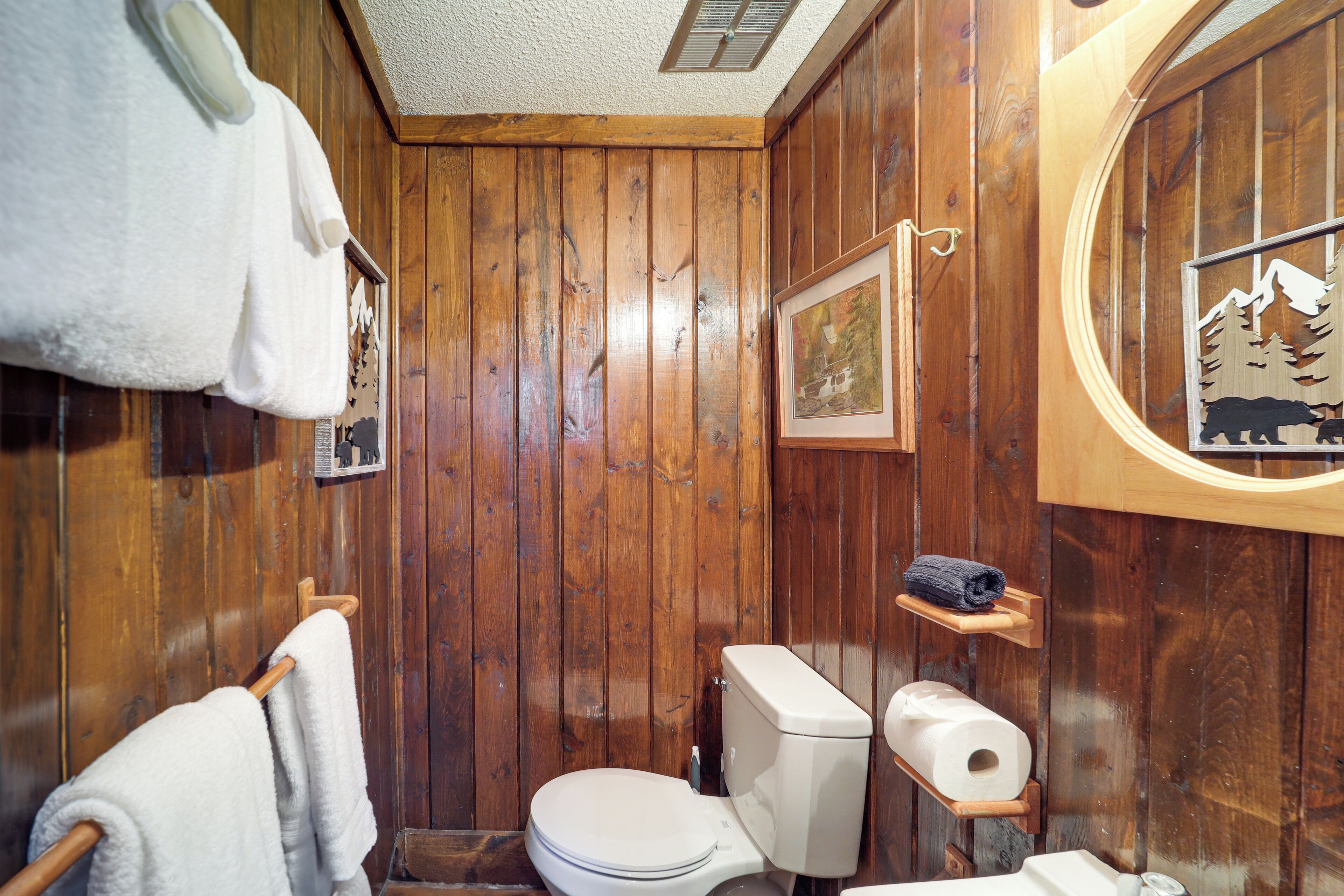 Une salle de bain aux murs lambrissés, équipée de toilettes, d’un porte-serviettes et de tableaux encadrés.