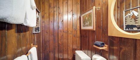 A wooden-paneled bathroom with a toilet, towel rack, and framed pictures on the walls.