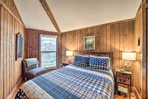 Une chambre à coucher aux murs lambrissés, avec un lit, deux tables de chevet, une chaise et une fenêtre.
