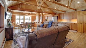 A spacious living area with a large leather sofa, wooden ceiling beams, and a kitchen in the background. - 'away at Moose Bay' Breezy Point Gem w/ Game Room (Pequot Lakes)